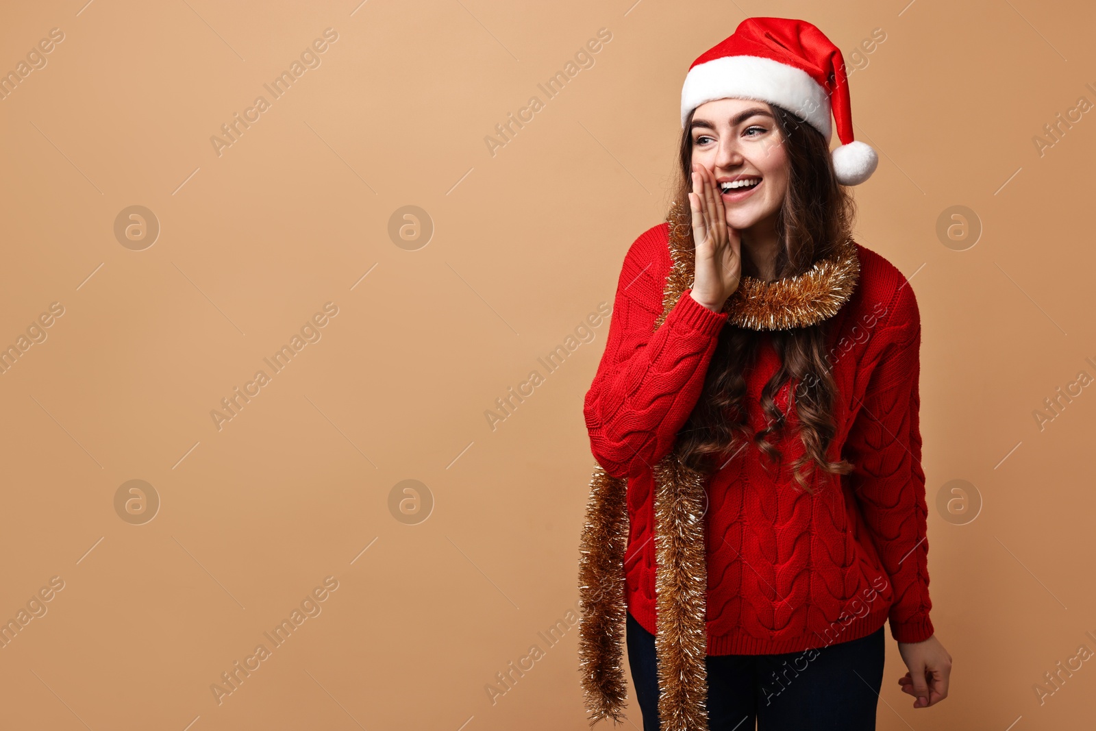 Photo of Happy young woman with tinsel and Santa hat on beige background. Space for text