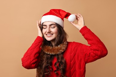 Photo of Happy young woman with tinsel and Santa hat on beige background