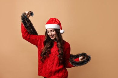 Photo of Happy young woman with tinsel and Santa hat on beige background. Space for text