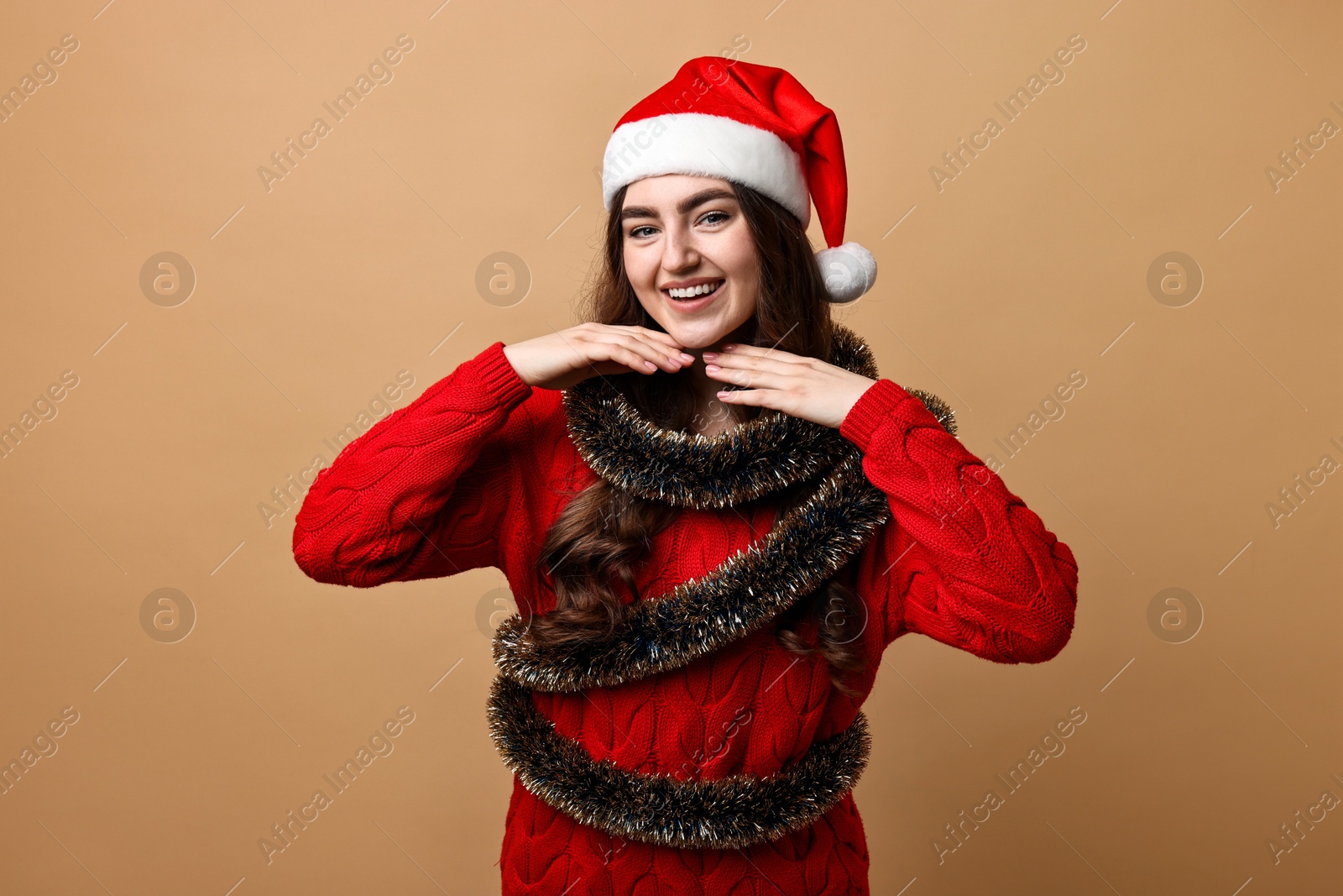 Photo of Happy young woman with tinsel and Santa hat on beige background