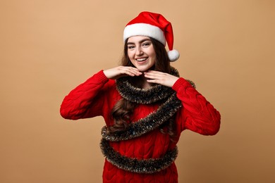 Photo of Happy young woman with tinsel and Santa hat on beige background