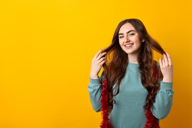 Photo of Happy young woman with tinsel on orange background. Space for text