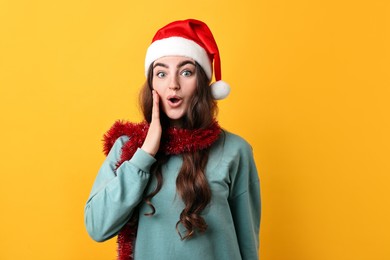 Photo of Emotional young woman with tinsel and Santa hat on orange background