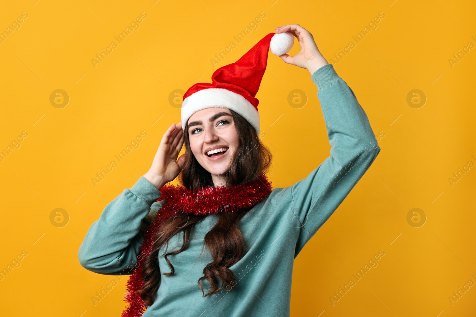 Photo of Happy young woman with tinsel and Santa hat on orange background