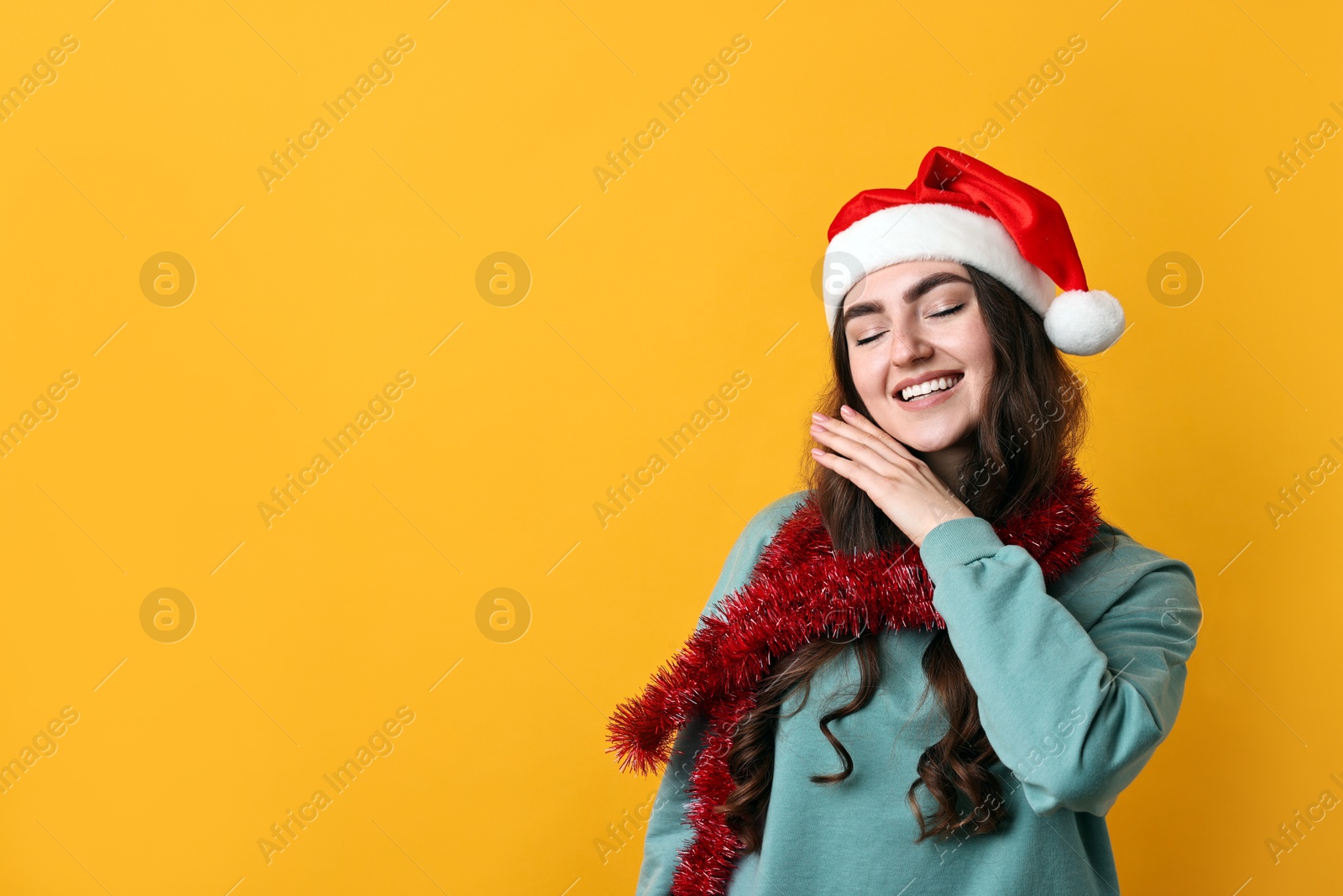 Photo of Happy young woman with tinsel and Santa hat on orange background. Space for text