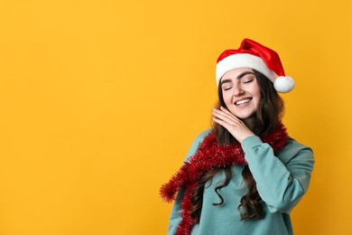 Photo of Happy young woman with tinsel and Santa hat on orange background. Space for text