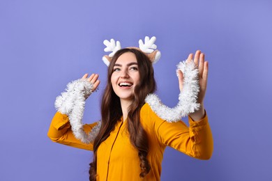 Photo of Happy young woman in reindeer headband with tinsel on purple background