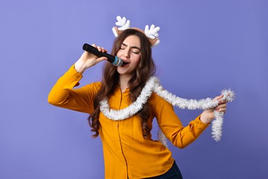 Photo of Young woman in reindeer headband with tinsel singing on purple background