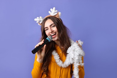 Photo of Young woman in reindeer headband with tinsel singing on purple background