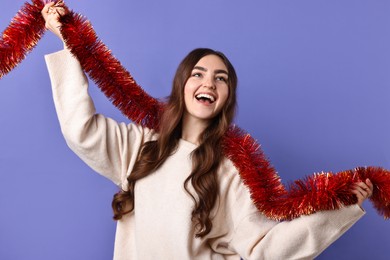 Photo of Happy young woman with tinsel on purple background