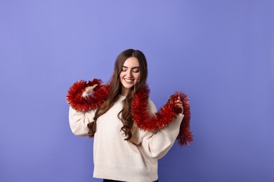 Photo of Happy young woman with tinsel on purple background