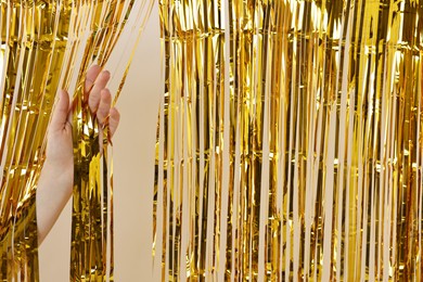 Photo of Woman near golden foil curtain against beige background, closeup