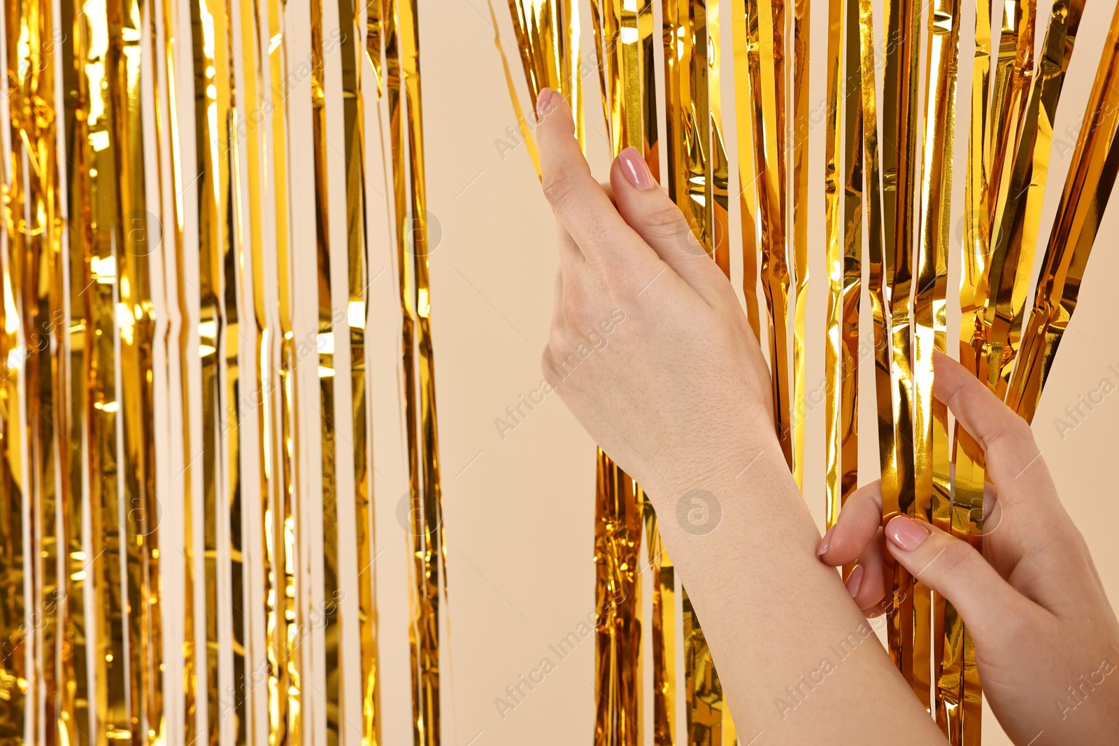 Photo of Woman near golden foil curtain against beige background, closeup