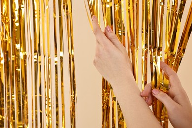 Photo of Woman near golden foil curtain against beige background, closeup