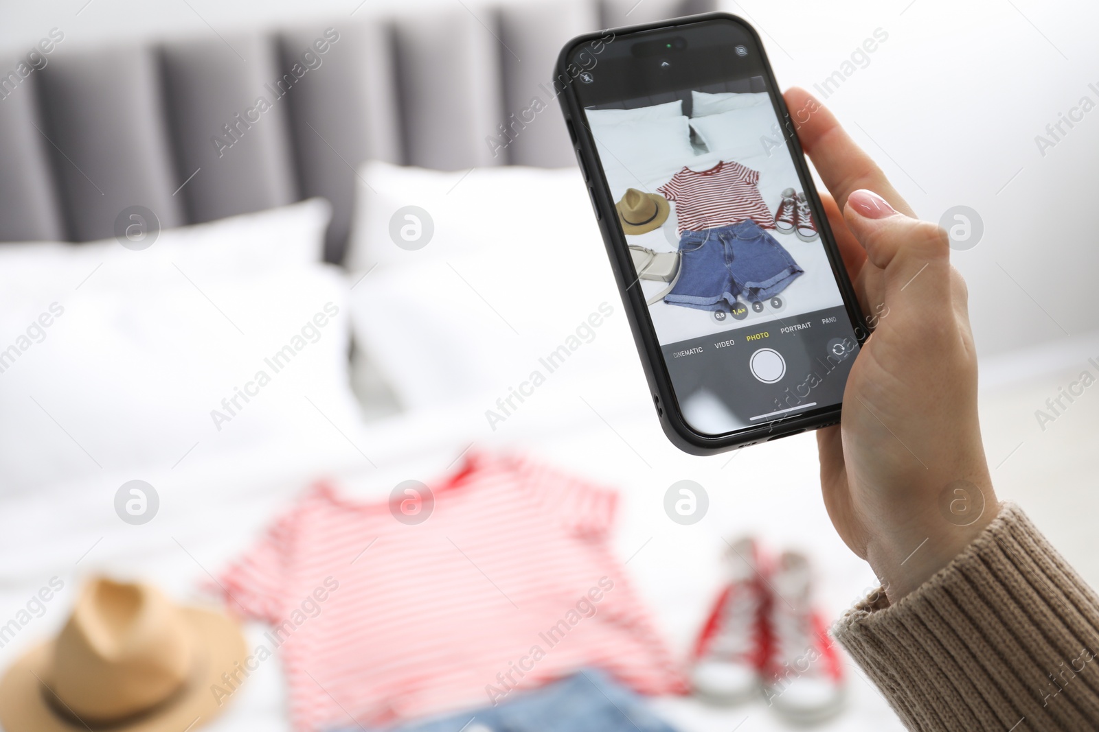 Photo of Woman with smartphone taking photo of her used clothes indoors, selective focus