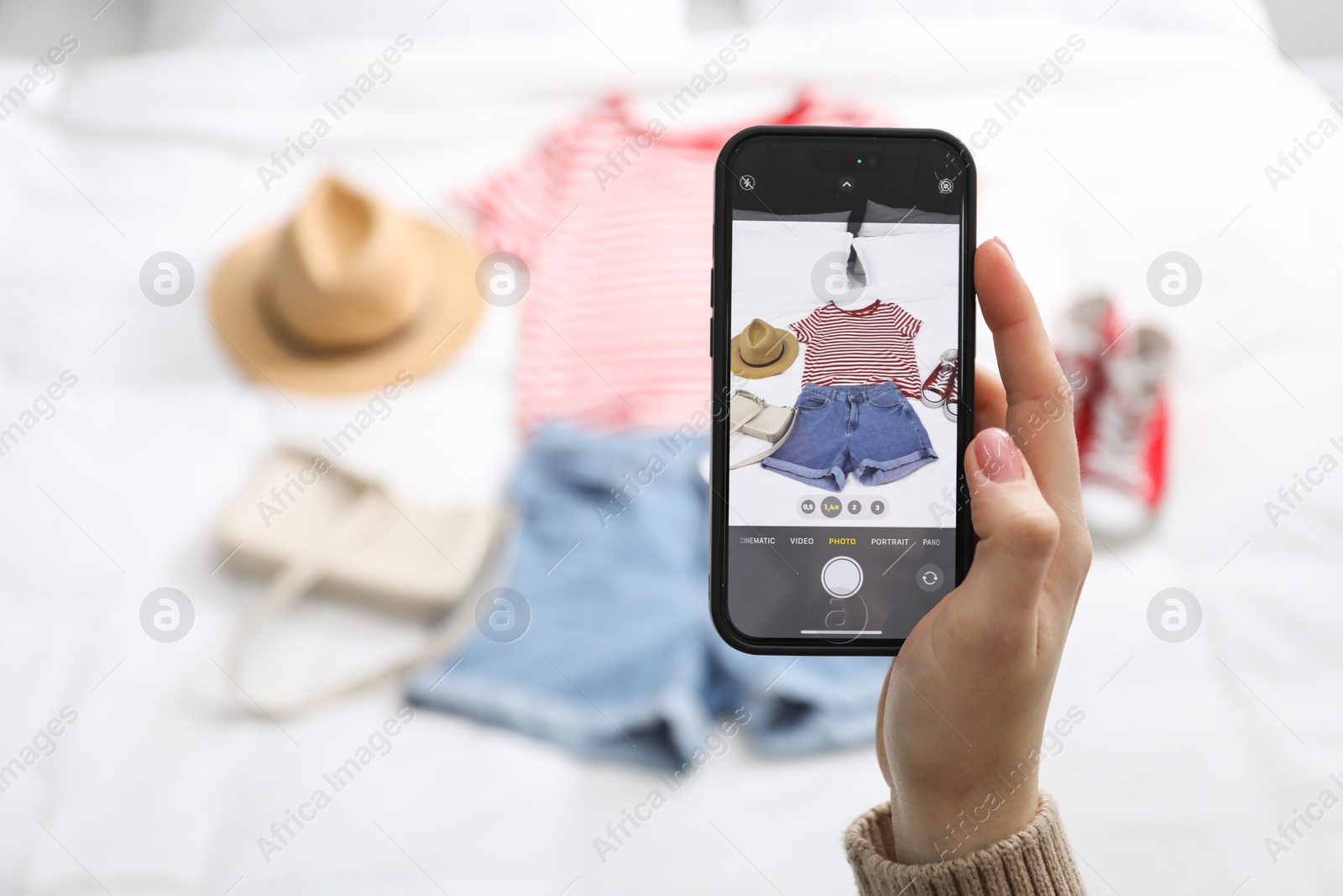 Photo of Woman with smartphone taking photo of her used clothes indoors, selective focus