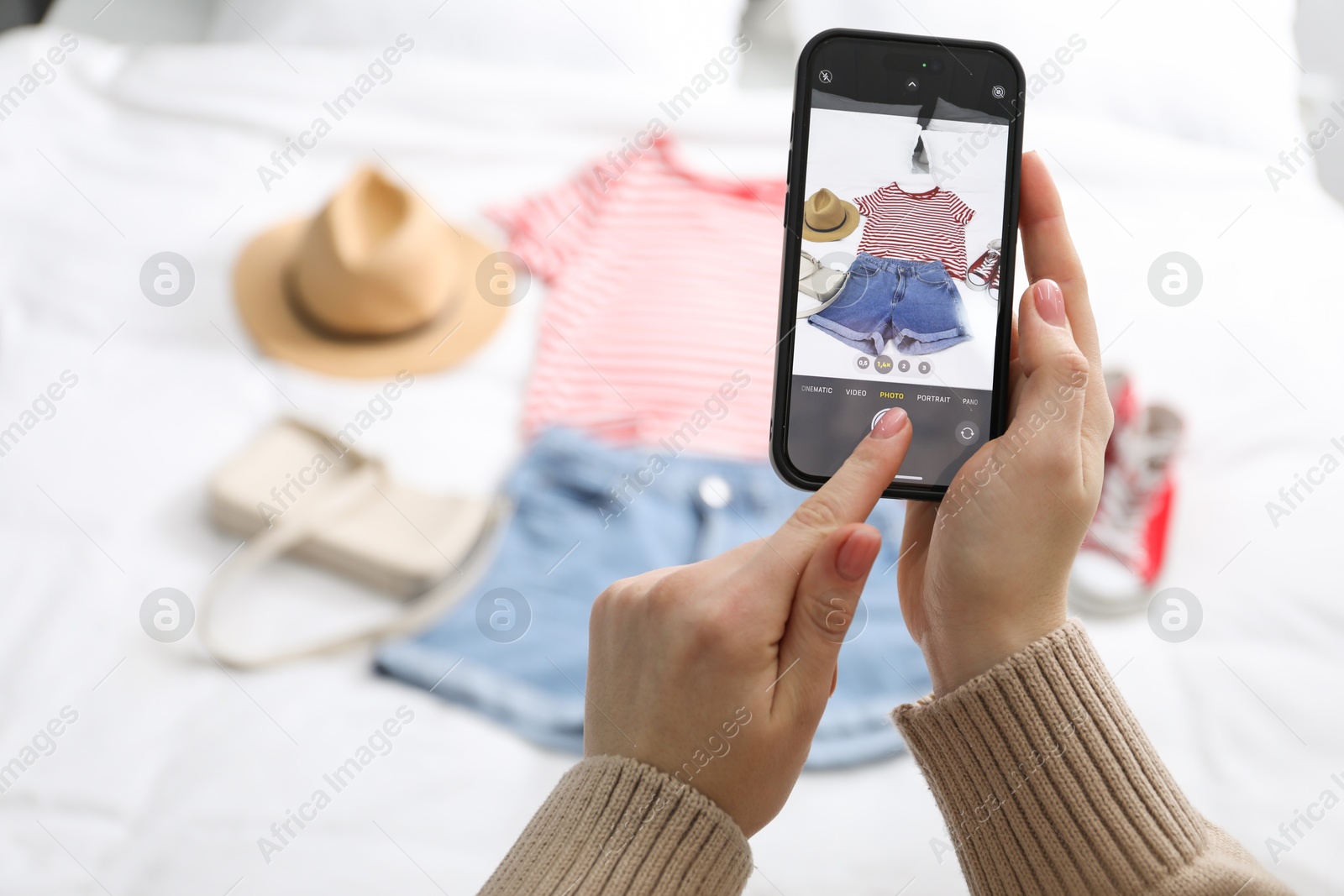 Photo of Woman with smartphone taking photo of her used clothes indoors, selective focus