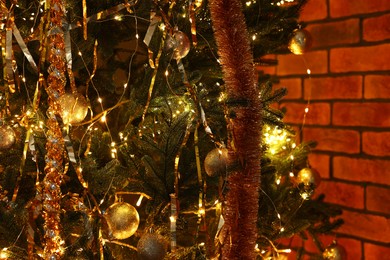 Photo of Shiny tinsels, baubles and festive lights on Christmas tree near brick wall, closeup