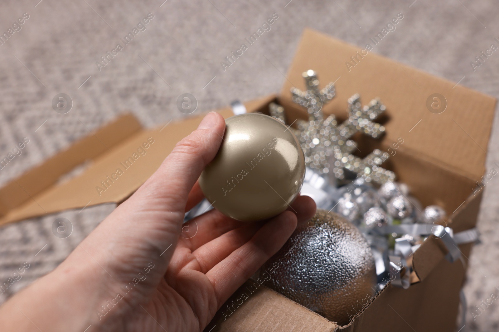 Photo of Woman holding bauble near box with other Christmas decor indoors, closeup