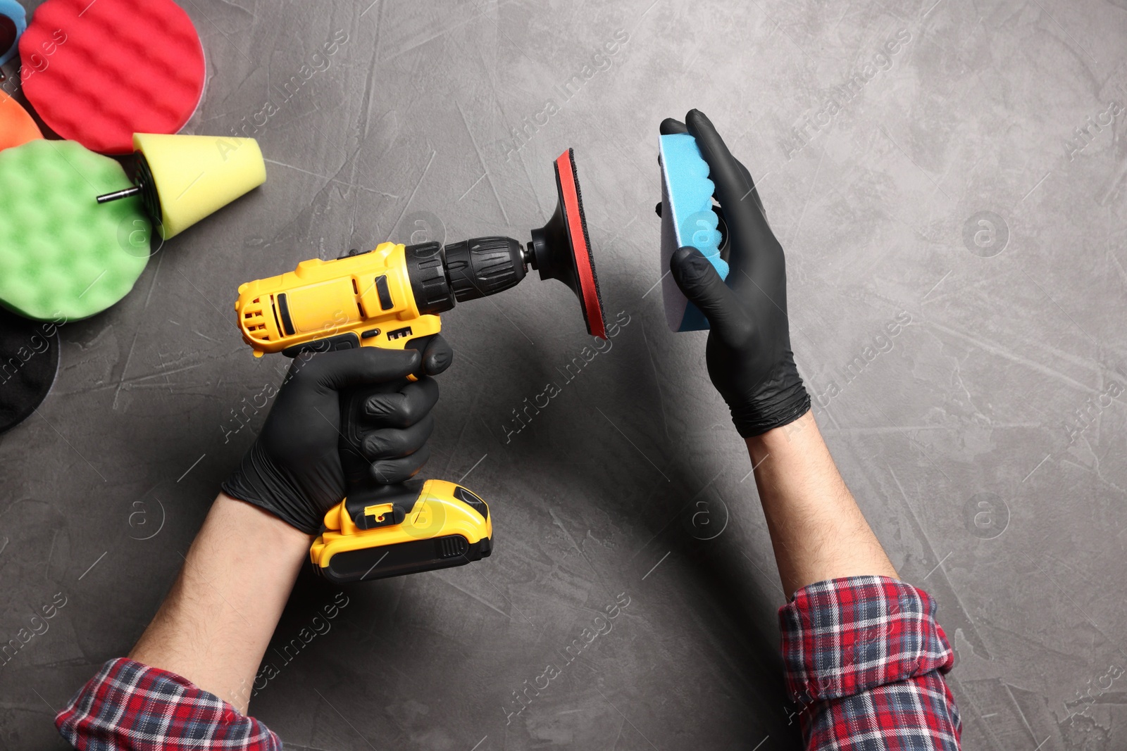 Photo of Man attaching polish pad onto electric screwdriver among colorful ones at grey textured table, top view