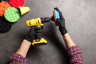 Photo of Man attaching polish pad onto electric screwdriver among colorful ones at grey textured table, top view