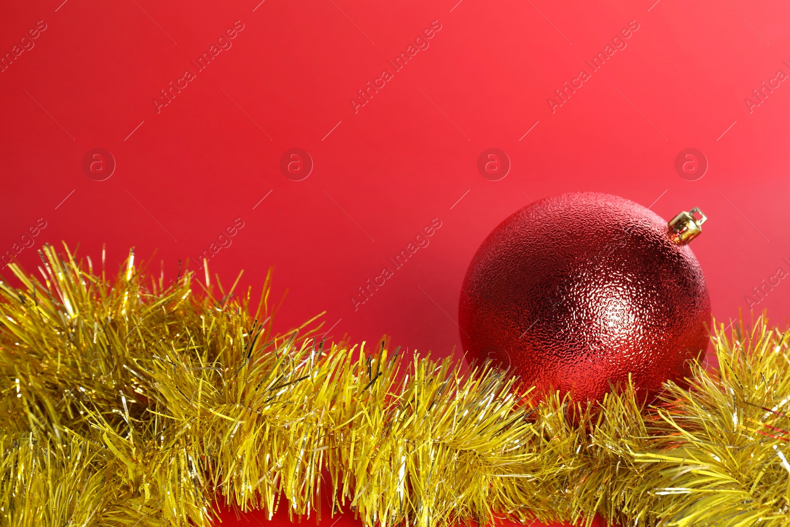 Photo of Beautiful Christmas ball and shiny tinsel on red background, space for text