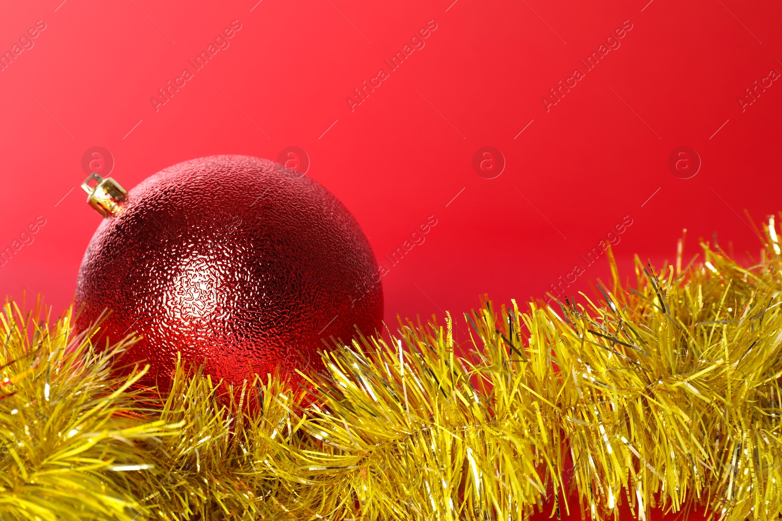 Photo of Beautiful Christmas ball and shiny tinsel on red background, closeup. Space for text