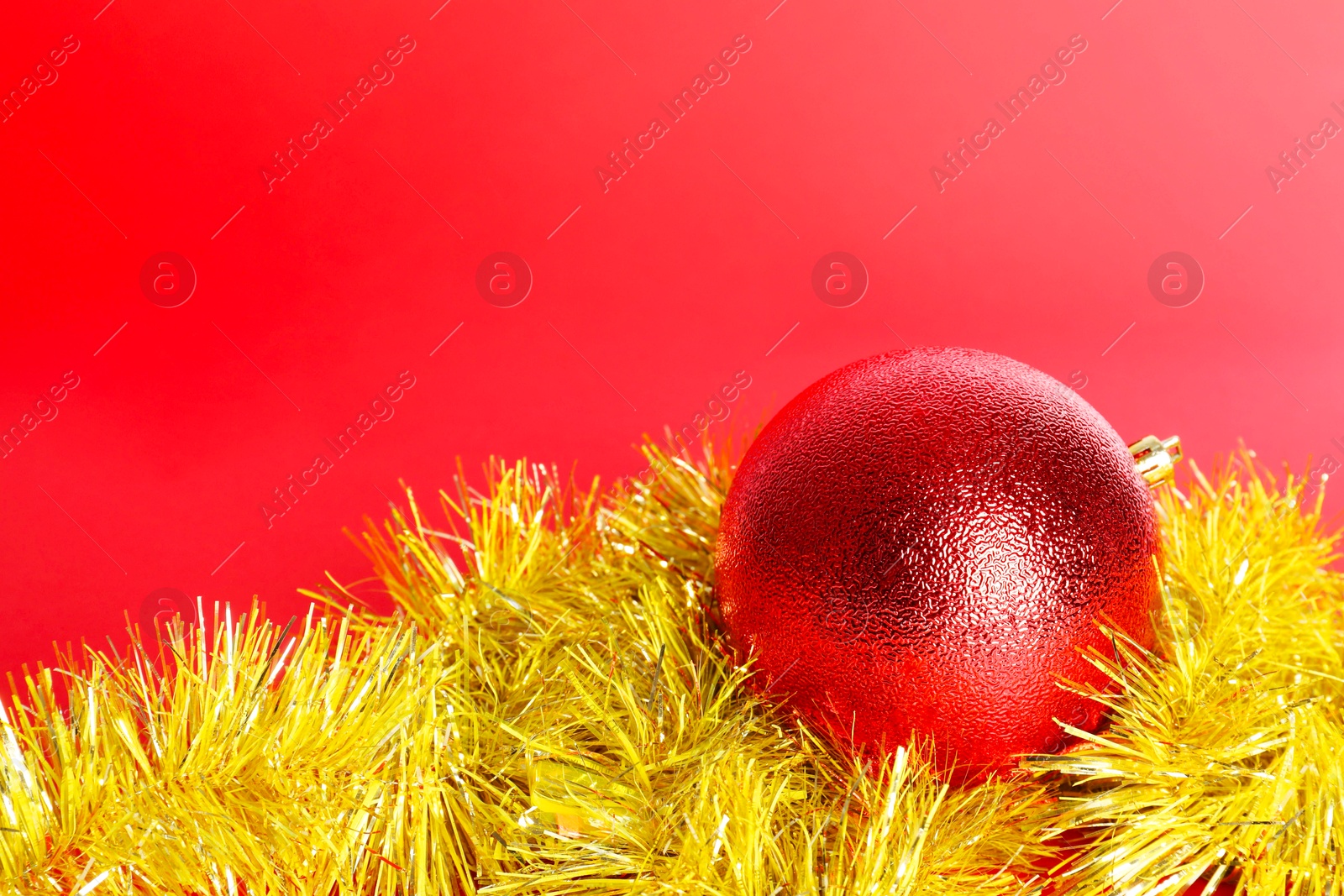 Photo of Beautiful Christmas ball and shiny tinsel on red background, closeup. Space for text