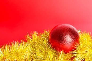 Photo of Beautiful Christmas ball and shiny tinsel on red background, closeup. Space for text