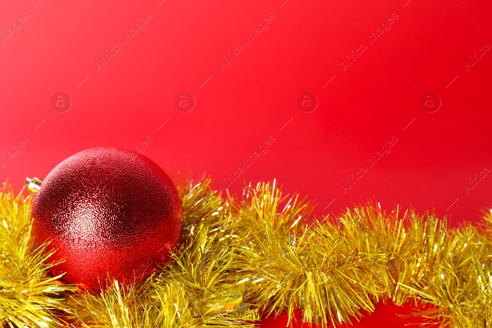 Photo of Beautiful Christmas ball and shiny tinsel on red background, space for text