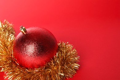 Photo of Beautiful Christmas ball and shiny tinsel on red background, closeup. Space for text