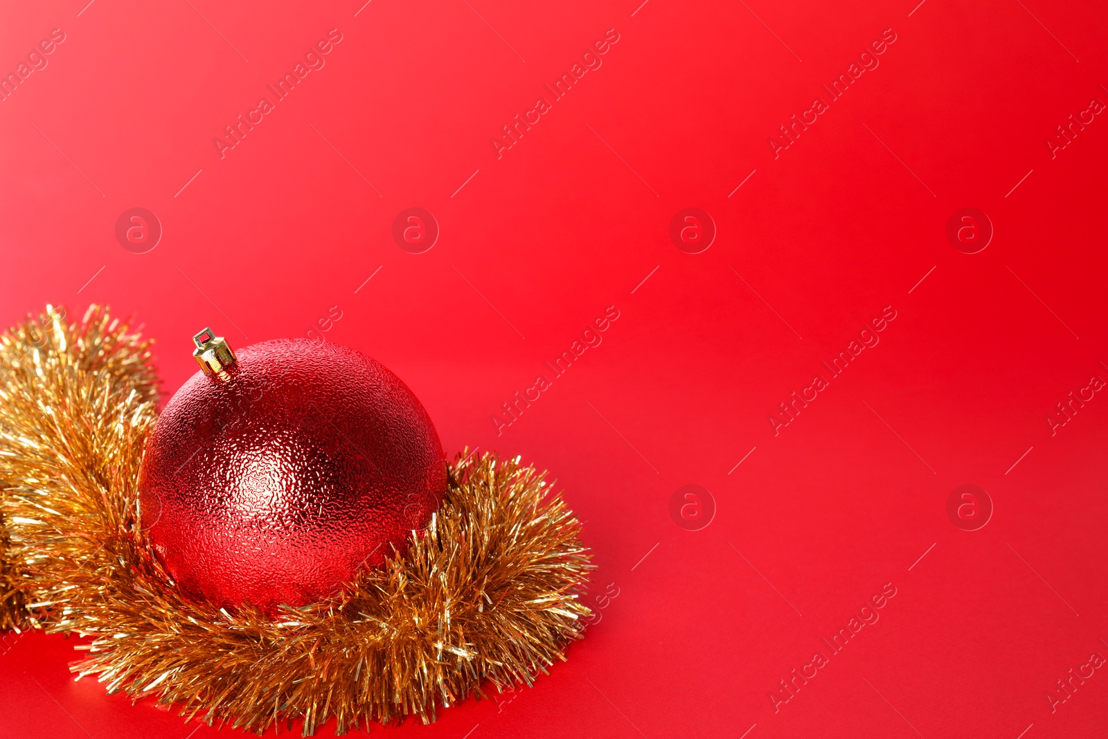 Photo of Beautiful Christmas ball and shiny tinsel on red background, space for text