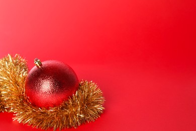 Photo of Beautiful Christmas ball and shiny tinsel on red background, space for text