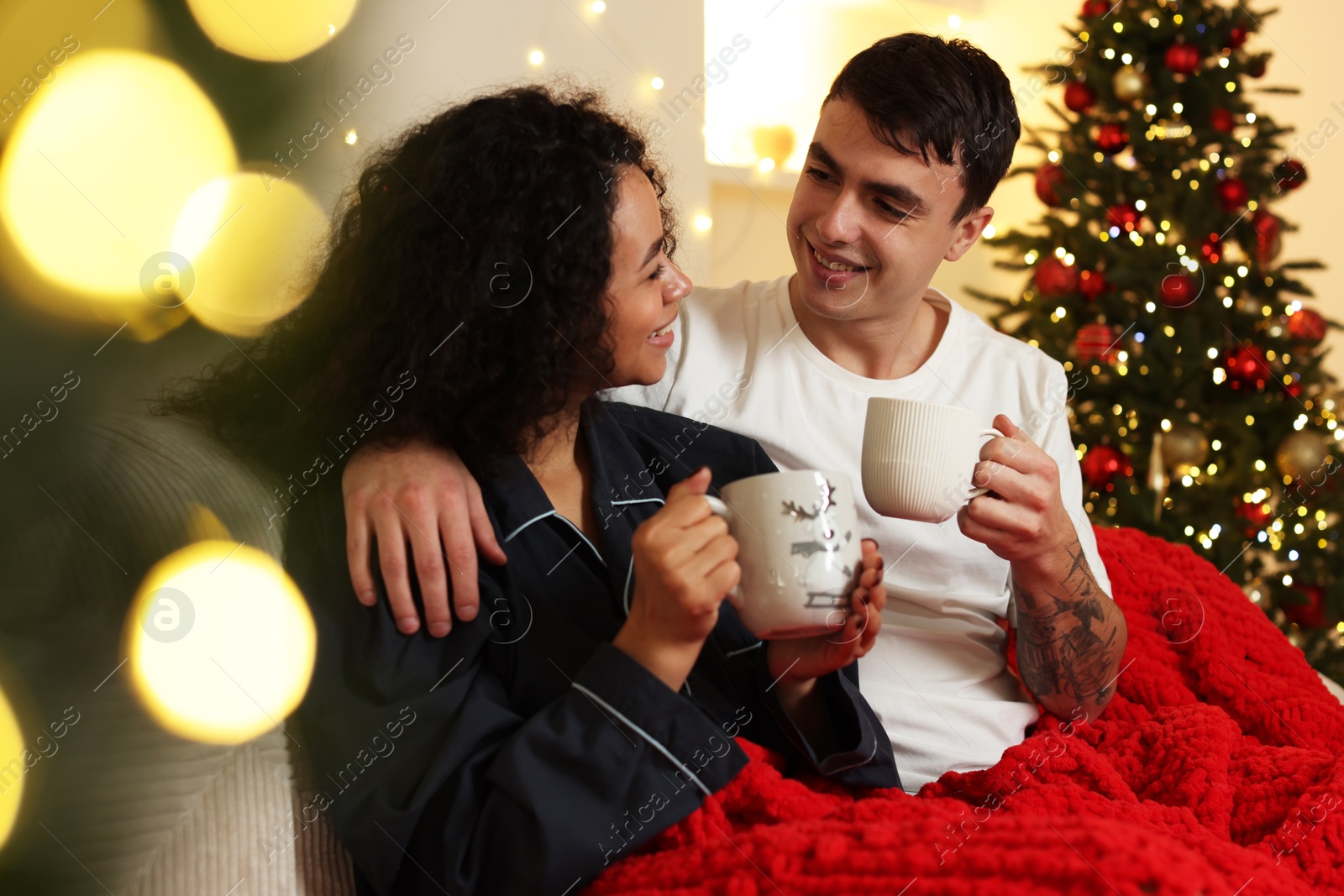 Photo of Happy couple with mugs of drinks spending time together at home. Christmas celebration