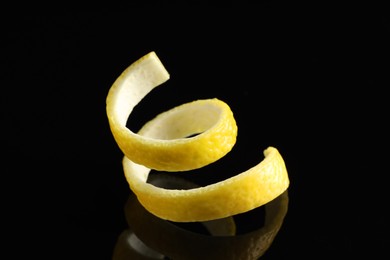 Photo of One curly lemon peel on black mirror surface, closeup