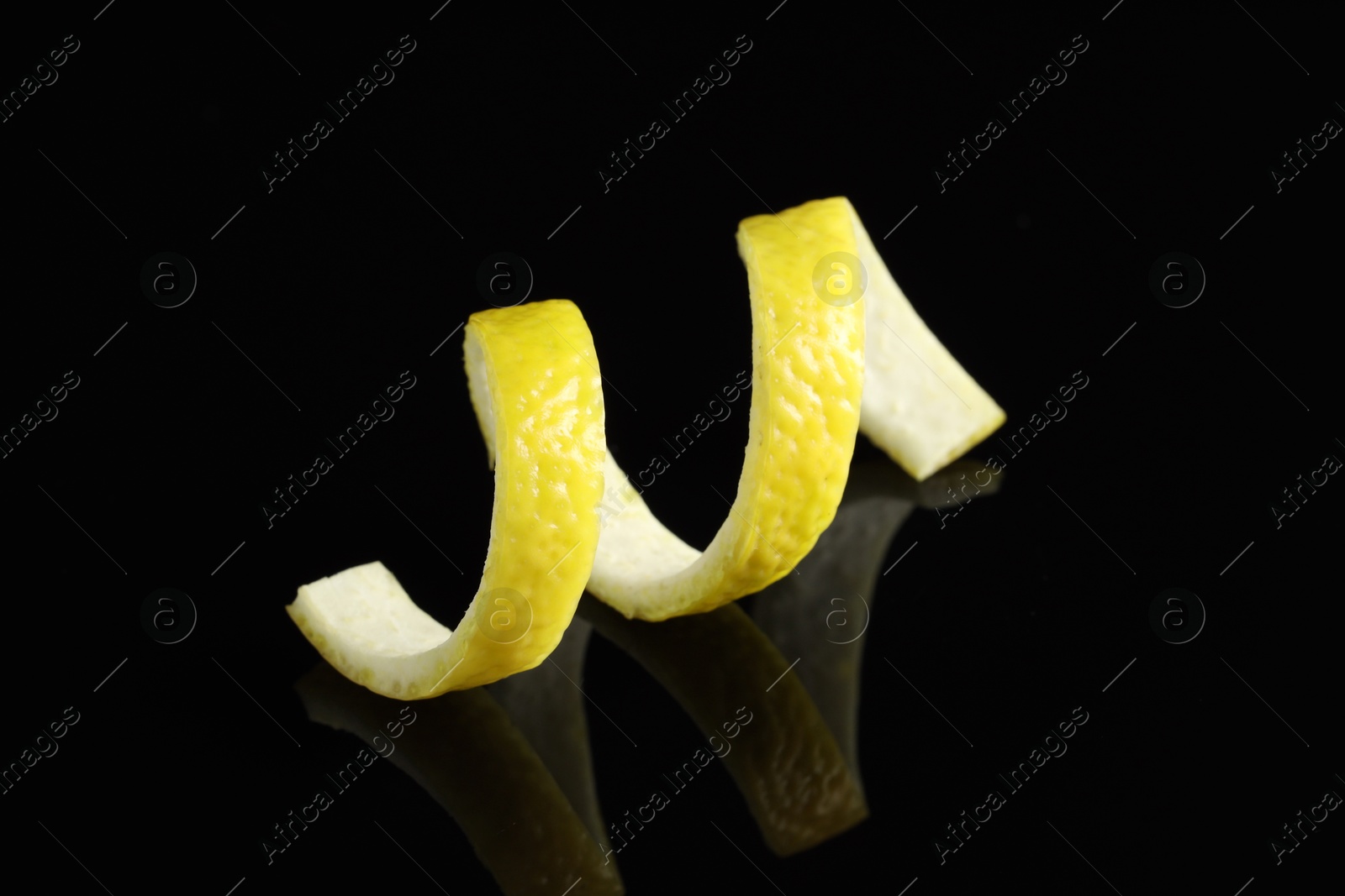 Photo of One curly lemon peel on black mirror surface, closeup