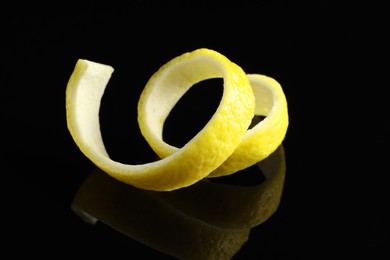 Photo of One curly lemon peel on black mirror surface, closeup