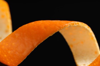 Photo of One curly orange peel on black background, macro view