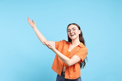 Photo of Happy woman welcoming friends or guests on light blue background