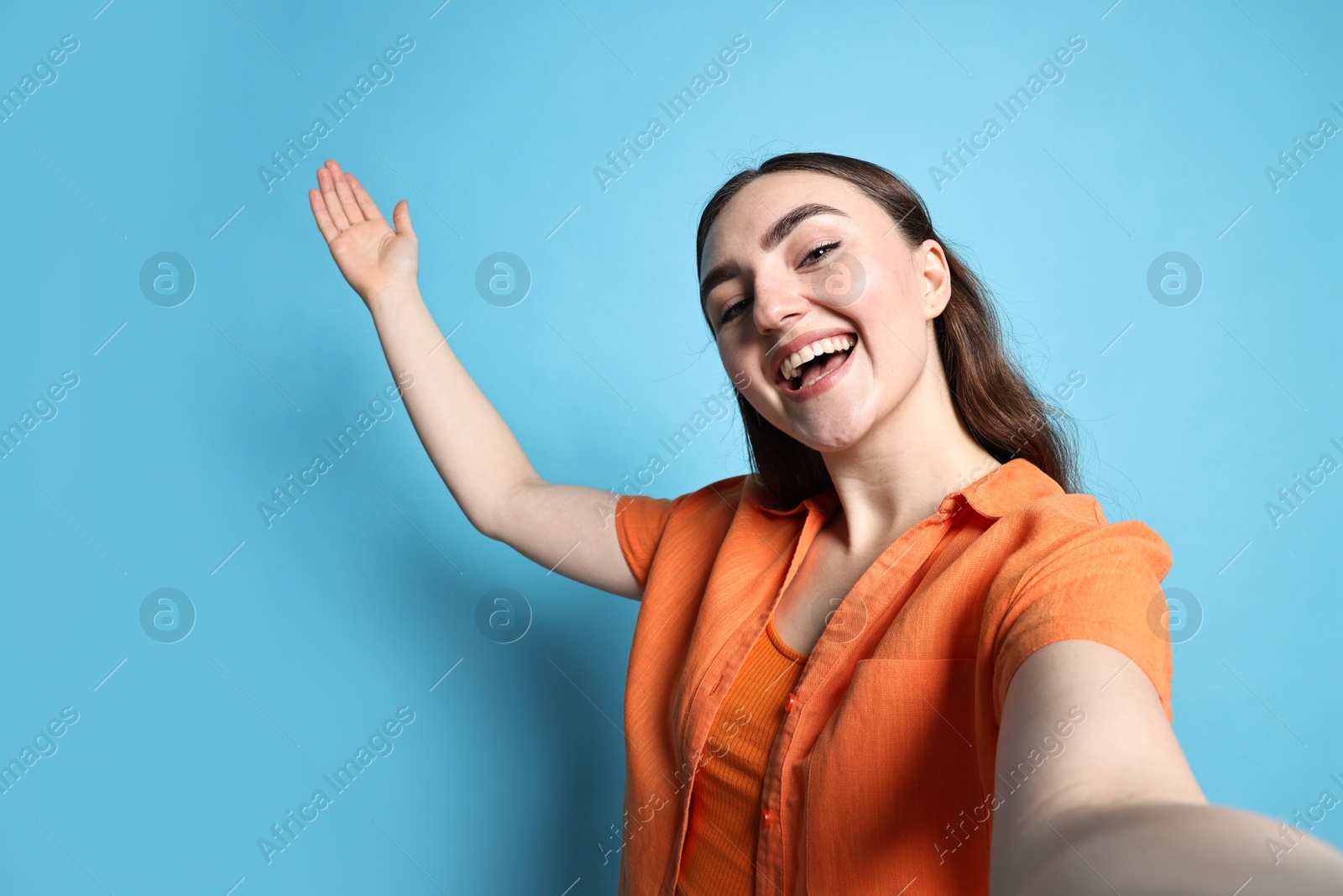 Photo of Happy woman welcoming friends or guests on blue background, view through front camera of gadget