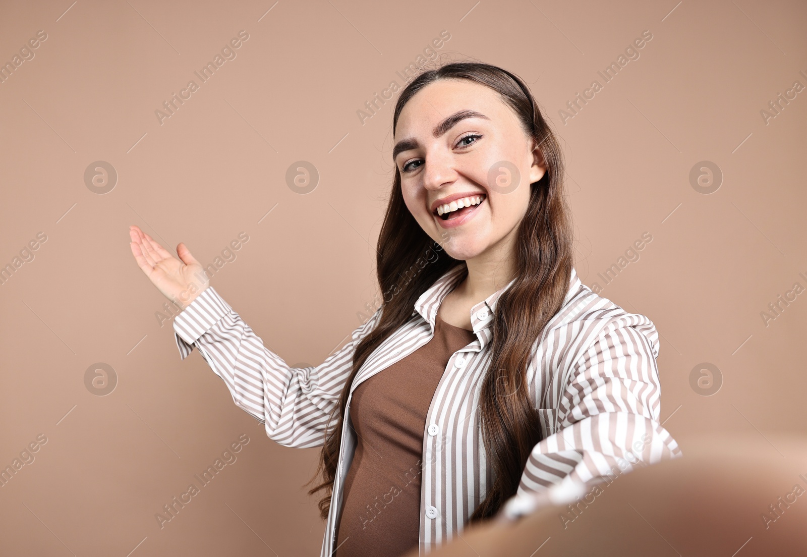 Photo of Happy woman taking selfie and welcoming friends or guests on beige background