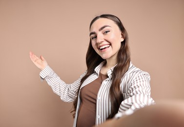 Photo of Happy woman taking selfie and welcoming friends or guests on beige background