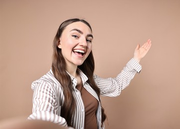 Photo of Happy woman taking selfie and welcoming friends or guests on beige background