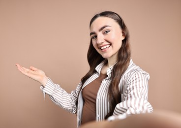 Photo of Happy woman taking selfie and welcoming friends or guests on beige background