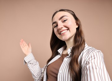 Photo of Happy woman taking selfie and welcoming friends or guests on beige background