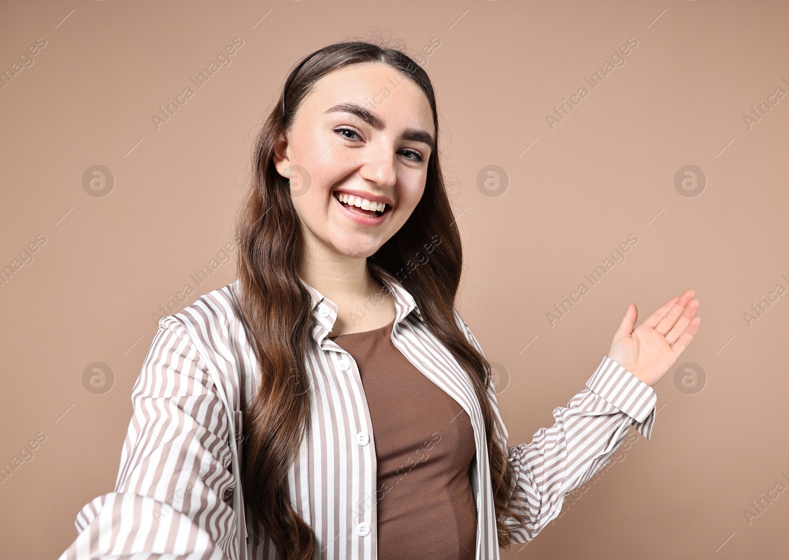 Photo of Happy woman taking selfie and welcoming friends or guests on beige background