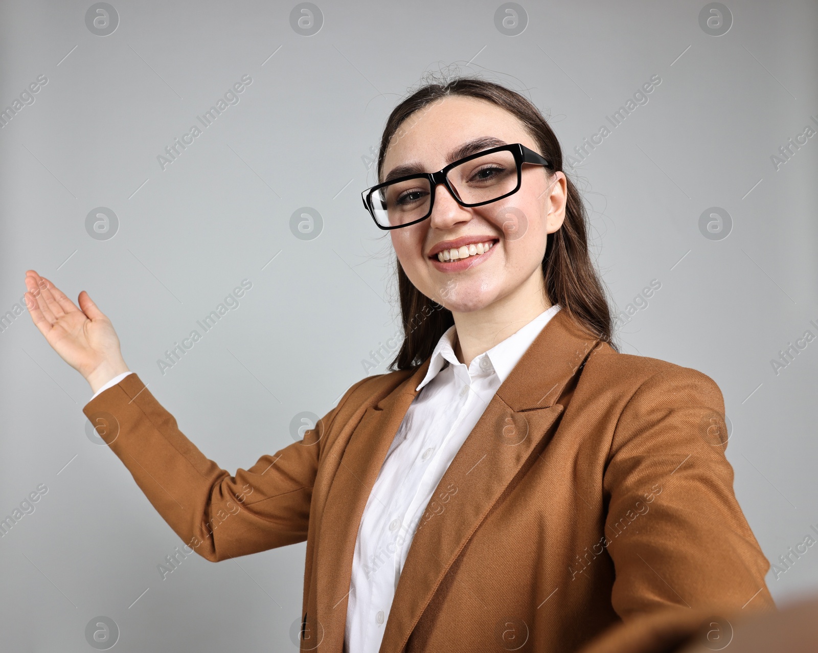 Photo of Happy businesswoman welcoming clients or partners by video call on grey background, view through camera