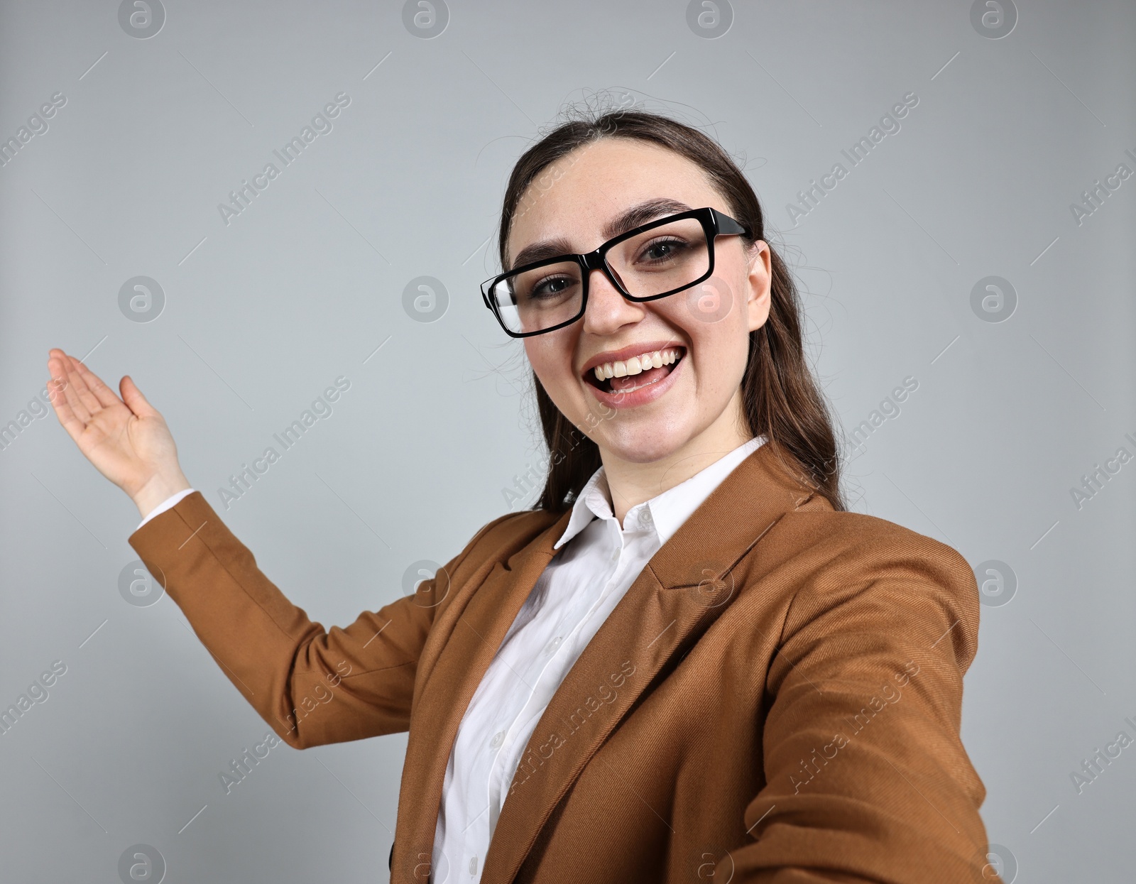 Photo of Happy businesswoman welcoming clients or partners by video call on grey background, view through camera