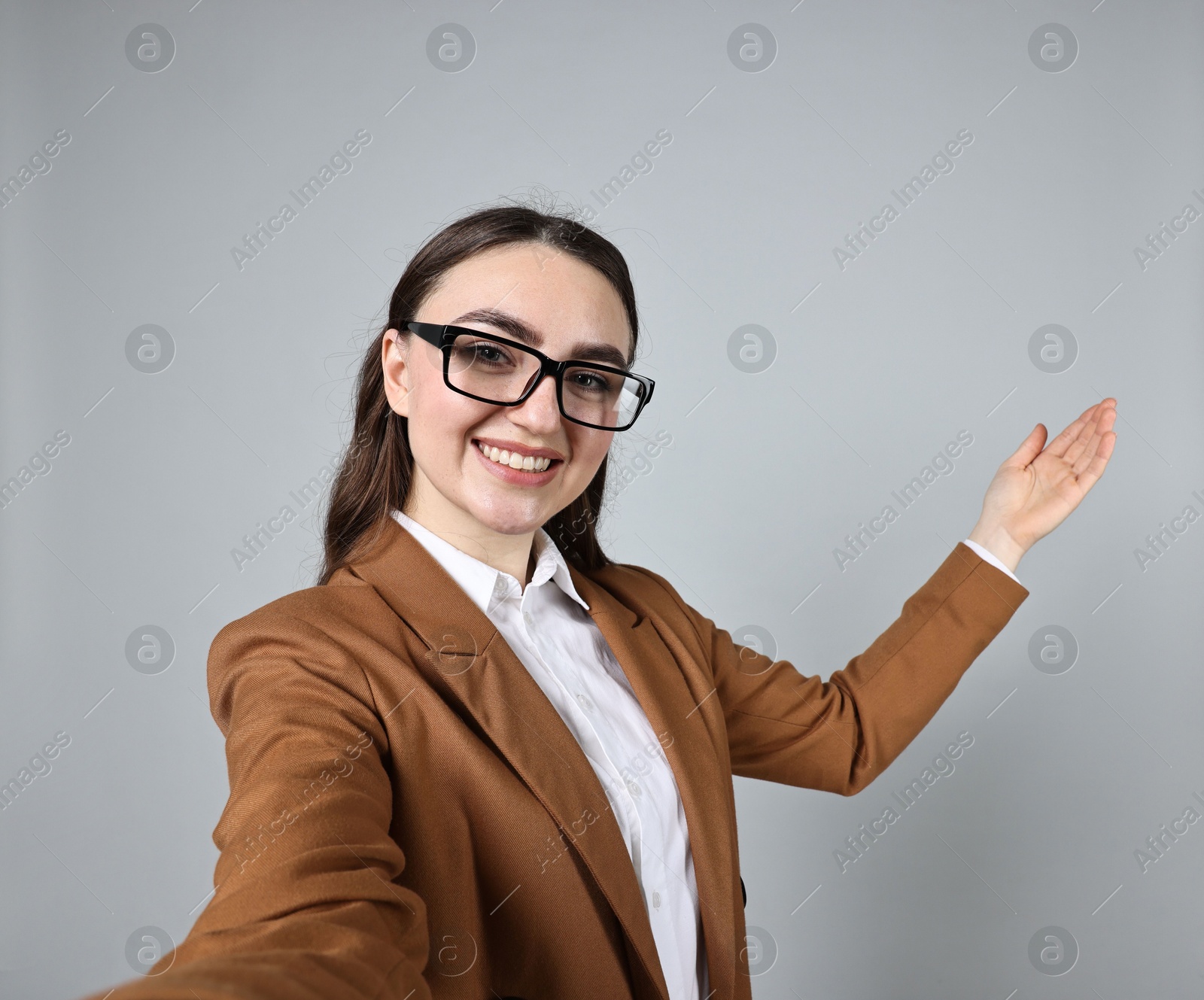 Photo of Happy businesswoman welcoming clients or partners by video call on grey background, view through camera