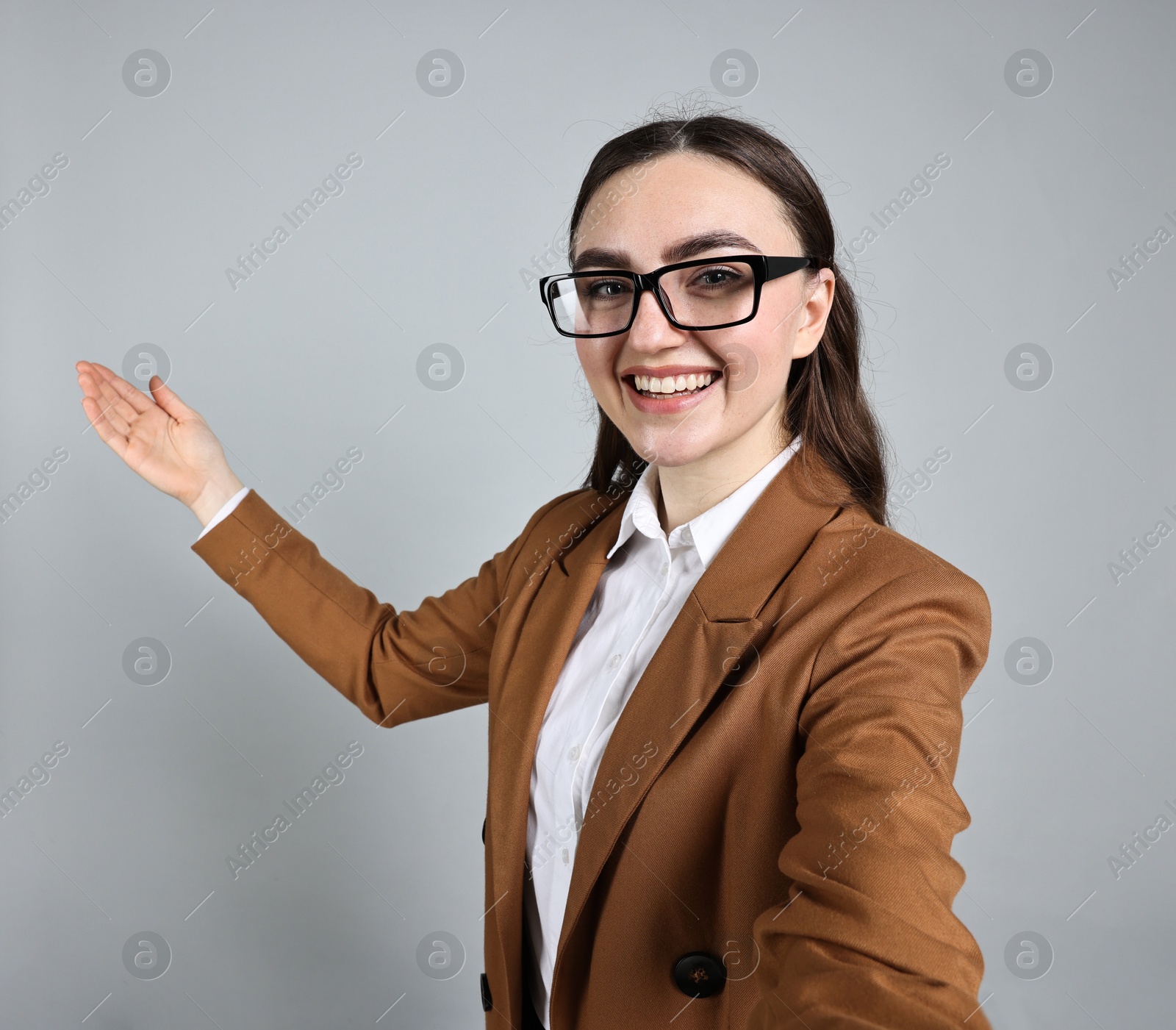 Photo of Happy businesswoman welcoming clients or partners by video call on grey background, view through camera